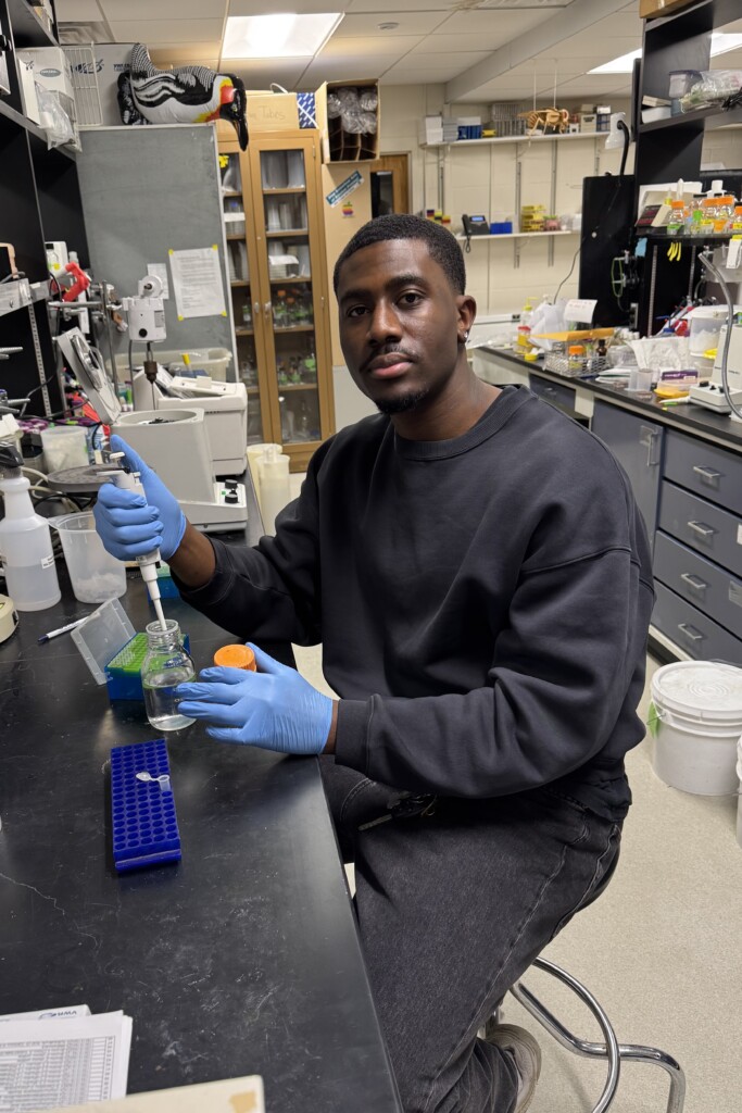 Photo of Dami Ajumobi sitting at a lab bench engaged in molecular biology